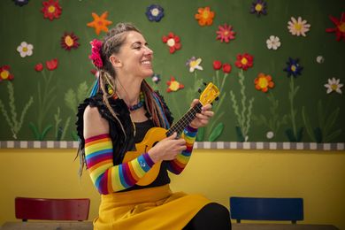 Mai Cocopelli mit Ukulele vor Blumenwand